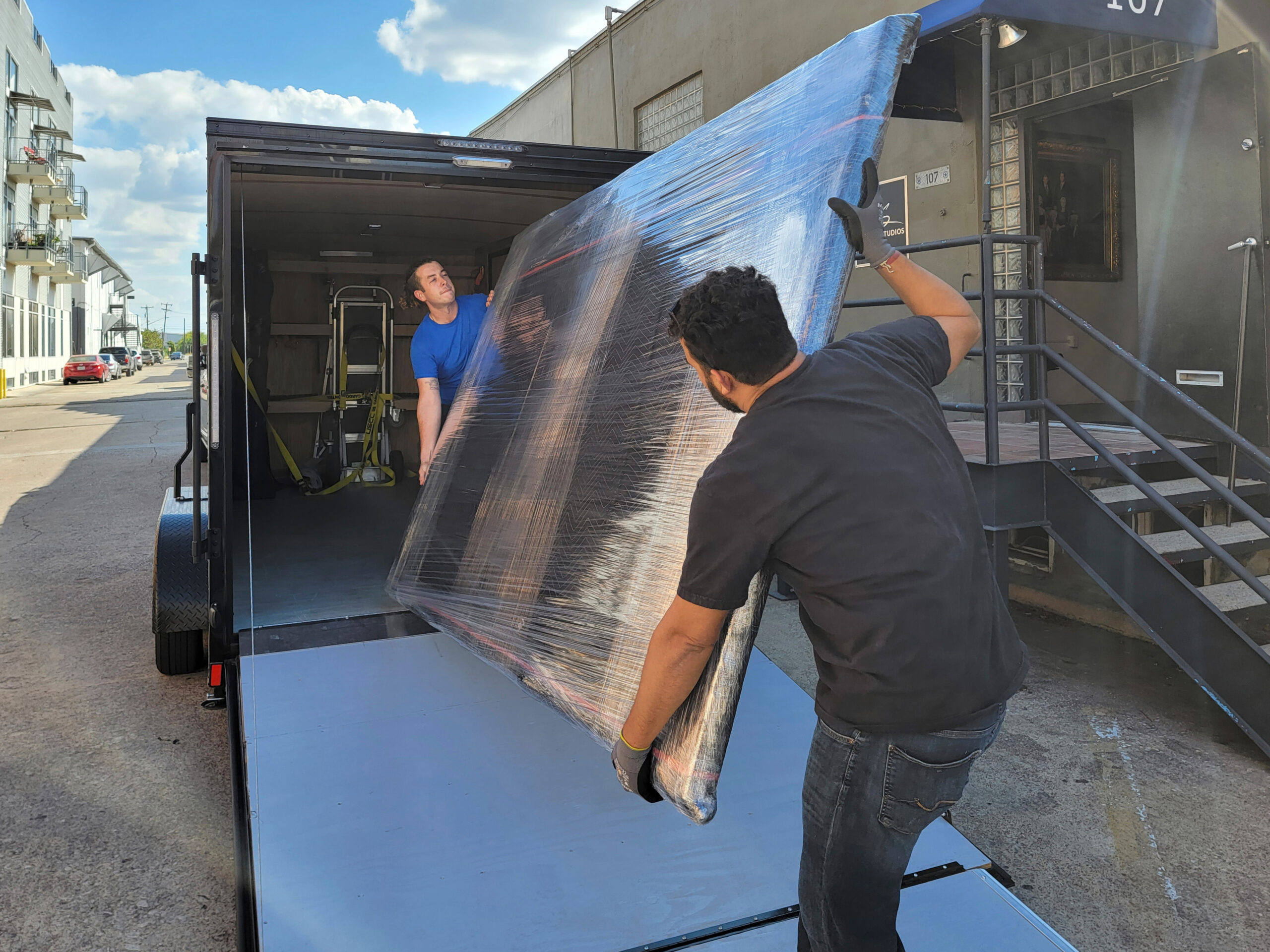 Two KGS Studios team members carefully loading a large, wrapped fine art piece onto a ramp into a custom art transport trailer, demonstrating white-glove delivery expertise.